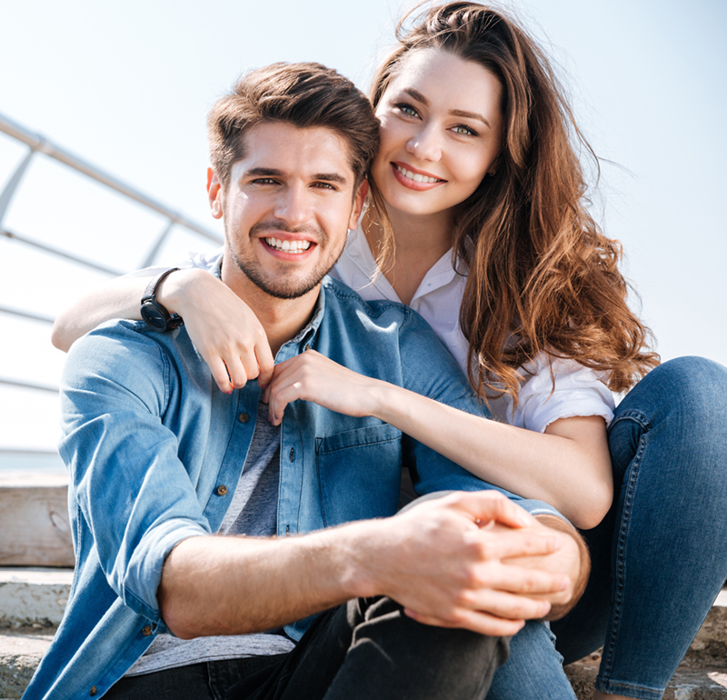Young couple laying on their backs on pavement looking up at camera with smiles.